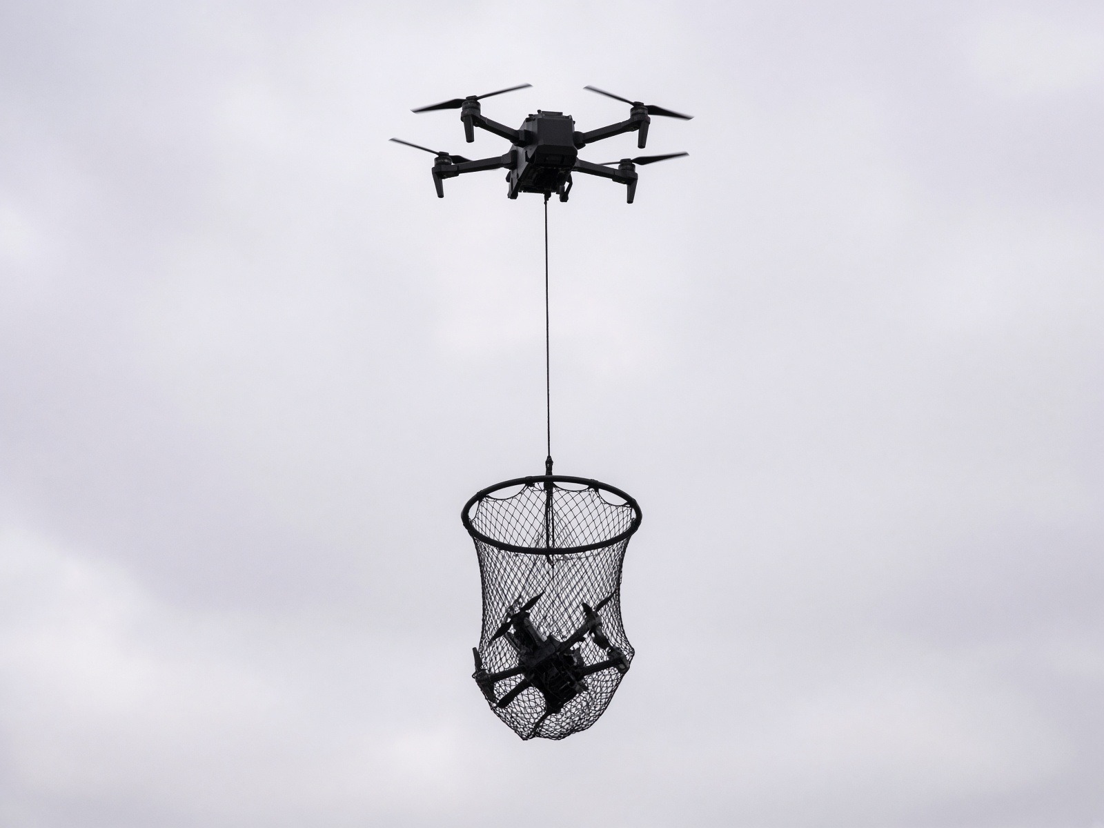 Interceptor aircraft with a circular hoop hanging on a vertical line, a small unmanned aircraft tangled in the net